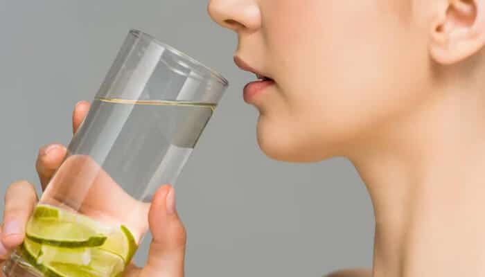 Woman drinking lime water for hydration, a natural method on How To Tighten Face Skin Naturally At Home.