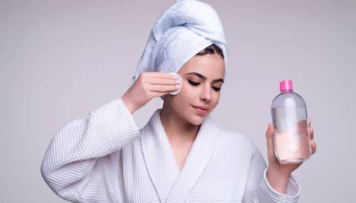 Woman in a bathrobe using a cotton pad and cleanser as part of the Korean Skincare Routine for clear and glowing skin.