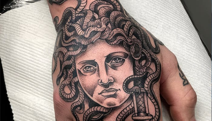 Black and grey Medusa tattoo on hand with intricate snake hair, representing resilience, power, and Medusa Tattoo Meaning.