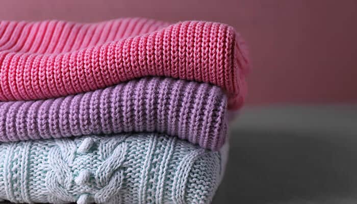 A stack of cozy, soft cashmere sweaters in pink, purple, and light blue, representing the best cashmere sweaters for comfort and style.