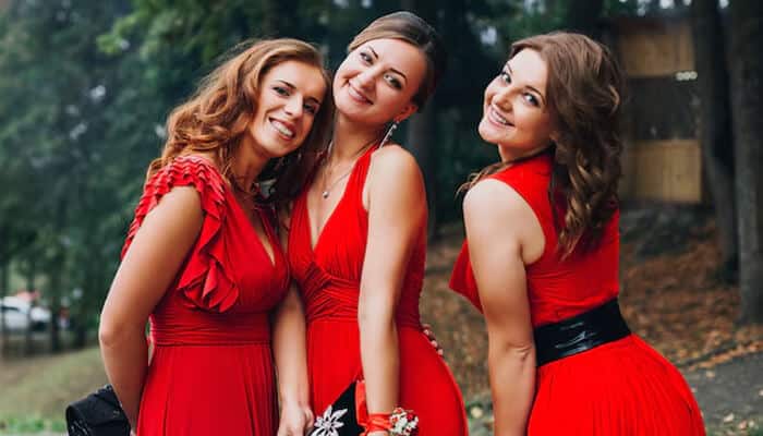 Three smiling women Wearing Red to a Wedding, posing outdoors in elegant red dresses.