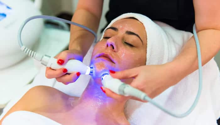 A woman undergoing a facial treatment for acne, with focus on clearing fungal acne vs closed comedones using advanced skincare techniques.