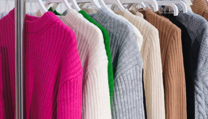 A collection of best cashmere sweaters in various colors like pink, white, green, gray, and brown hanging on a clothing rack, showcasing luxurious options.