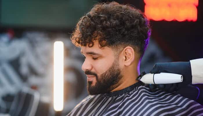 Low taper fade curly hair - Fashion in beauty - Fashion in Beauty Low Taper Fade on curly hair featuring neatly faded sides and back with defined natural curls on top, creating a clean, modern Low Taper Fade look during a professional barber session.