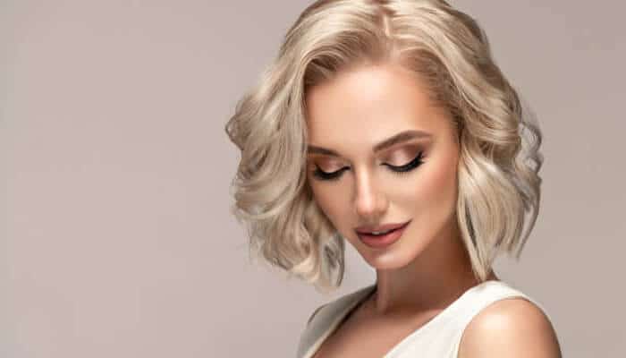 Understanding Bleached Blonde Hair - Fashion in beauty - Fashion in Beauty Portrait of a woman with short platinum blonde hair looking down, wearing a white sleeveless top.