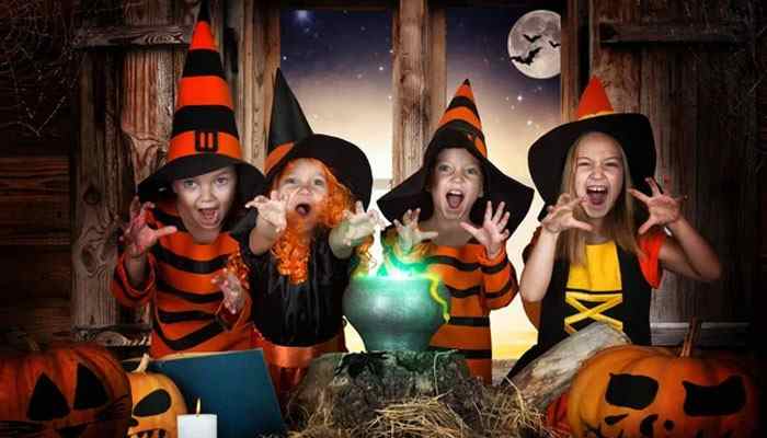 Costume Safety Tips for Kids - Fashion In Beauty - Fashion in Beauty Halloween Costumes for kids featuring four children dressed as witches with pointed hats, pumpkins, and a glowing cauldron in a spooky Halloween setting.