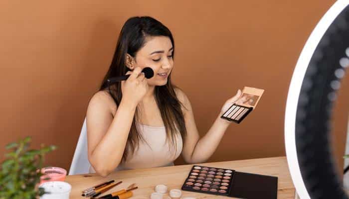 Is Fenty Beauty Worth Buying - Fashion In Beauty - Fashion in Beauty Woman applying makeup with a brush beside an eyeshadow palette and ring light, representing a Fenty Beauty routine focused on complexion, color, and personalized makeup application.